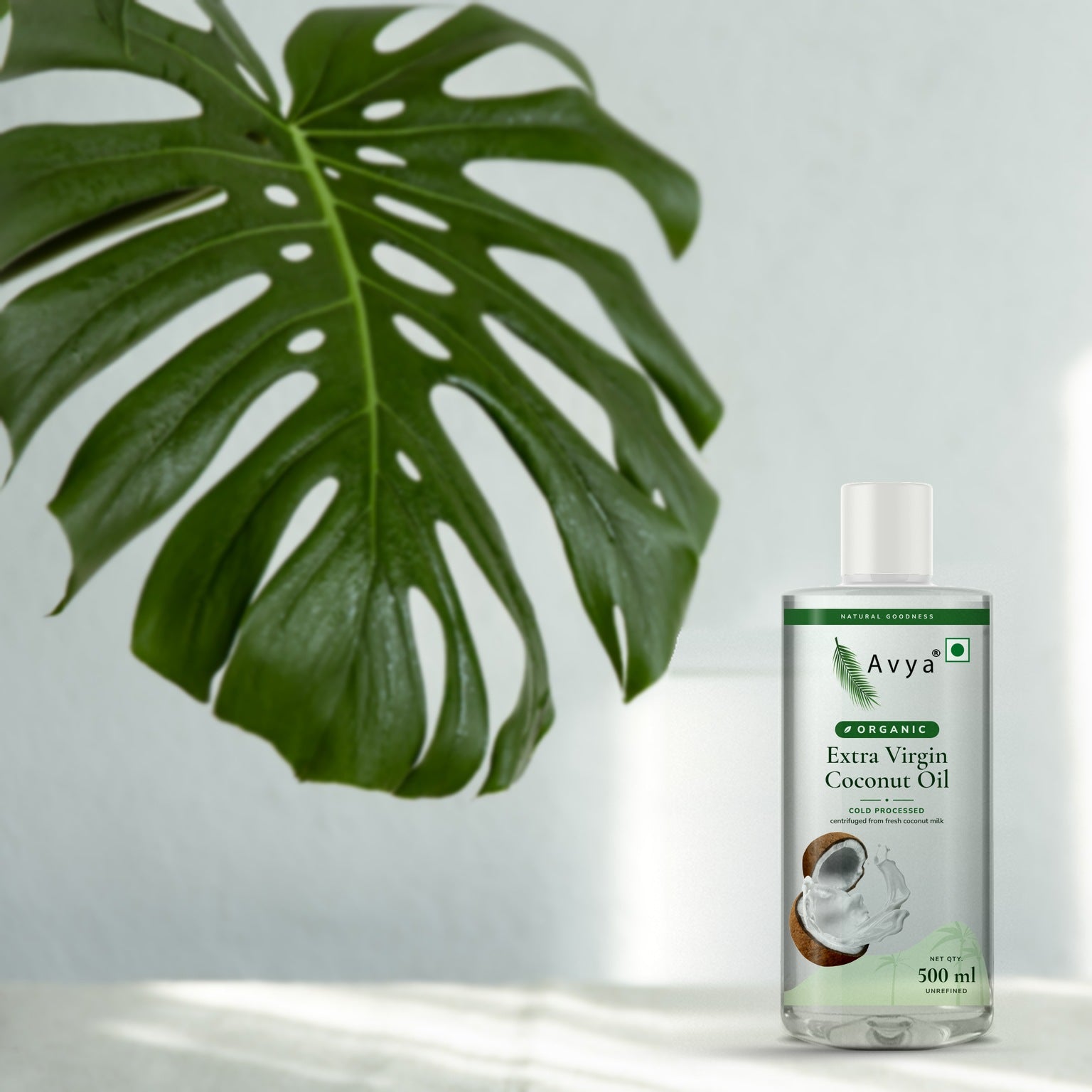 Avya Organic Extra Virgin Coconut Oil 500 ml with a monstera leaf in natural sunlight